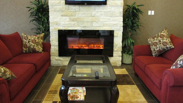 Una sala de estar con chimenea de piedra, un televisor de pantalla plana montado encima y dos sofás rojos con cojines estampados.