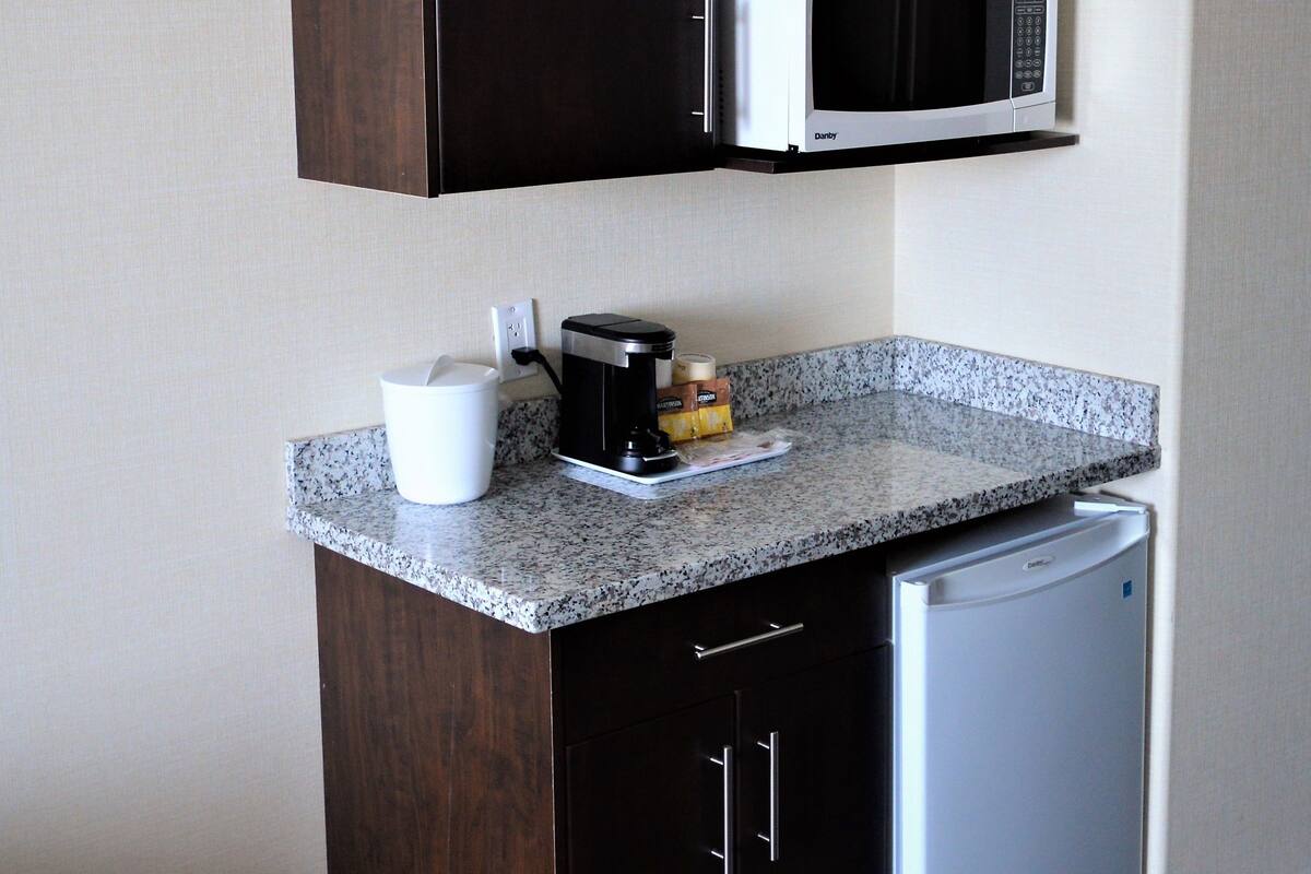 Een compacte kitchenette met donkere houten kastjes, een ingebouwde magnetron, een koffiezetapparaat en een kleine koelkast.
