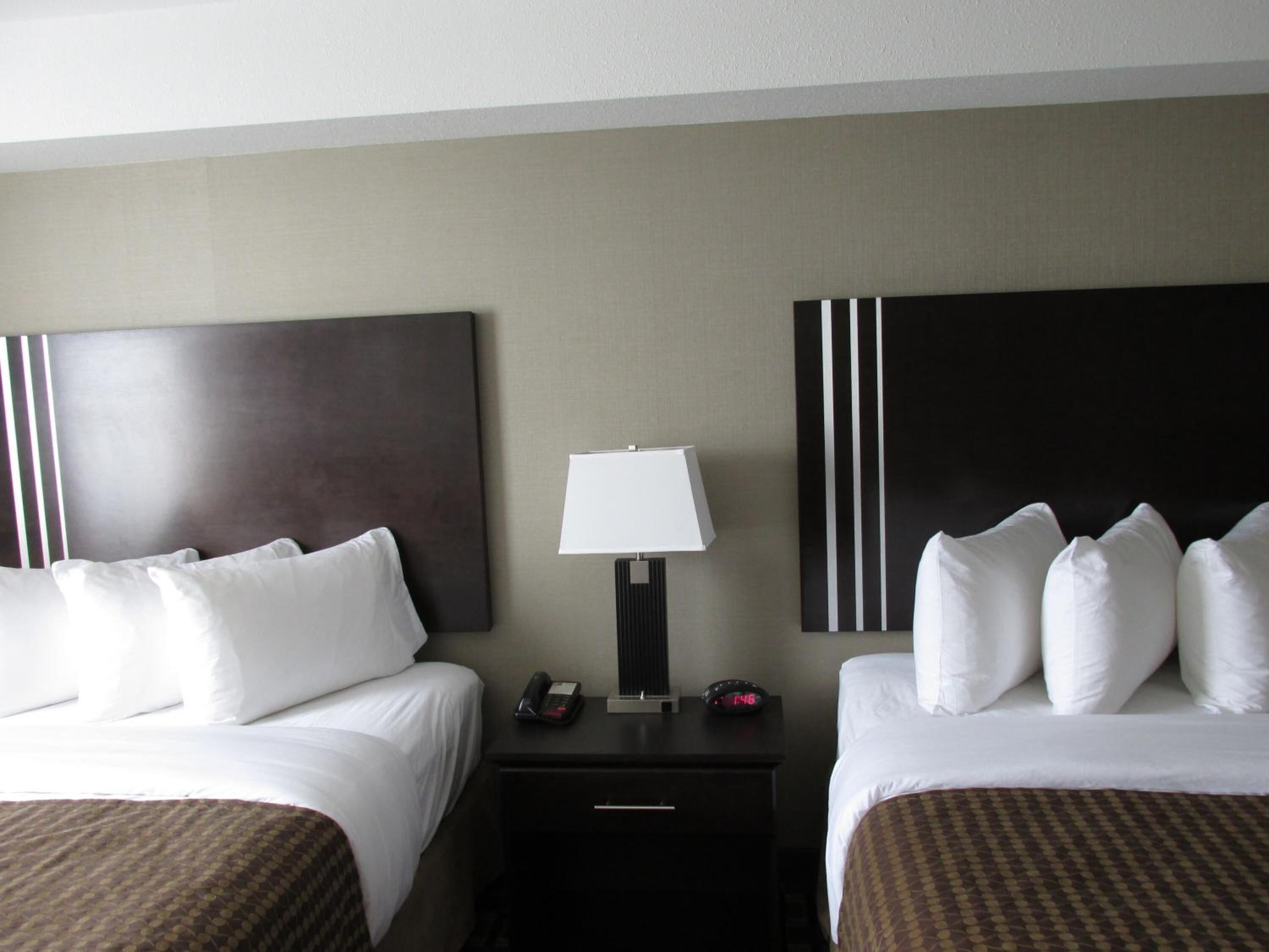 A hotel room with two beds, a nightstand with a lamp, a phone, and a clock.