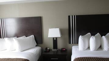A hotel room with two beds, a nightstand with a lamp, a phone, and a clock.