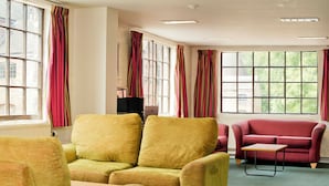 Una habitación con un sofá amarillo, un sofá rojo y una mesita. Hay ventanas grandes con cortinas.