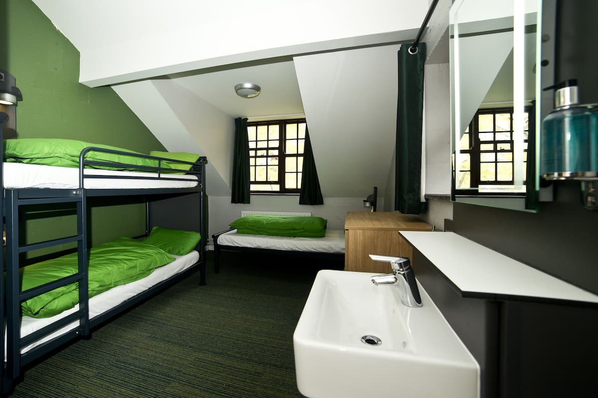 A dormitory room with bunk beds, a single bed, a sink, and a mirror.