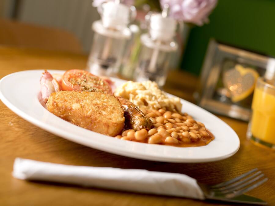 Un plato de comida con un cutlet rebozado, frijoles y tomate, junto a un vaso de jugo de naranja sobre una mesa de madera.