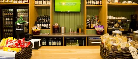 A bar area with shelves of liquor bottles, a television displaying a question, and a counter with snacks and condiments.