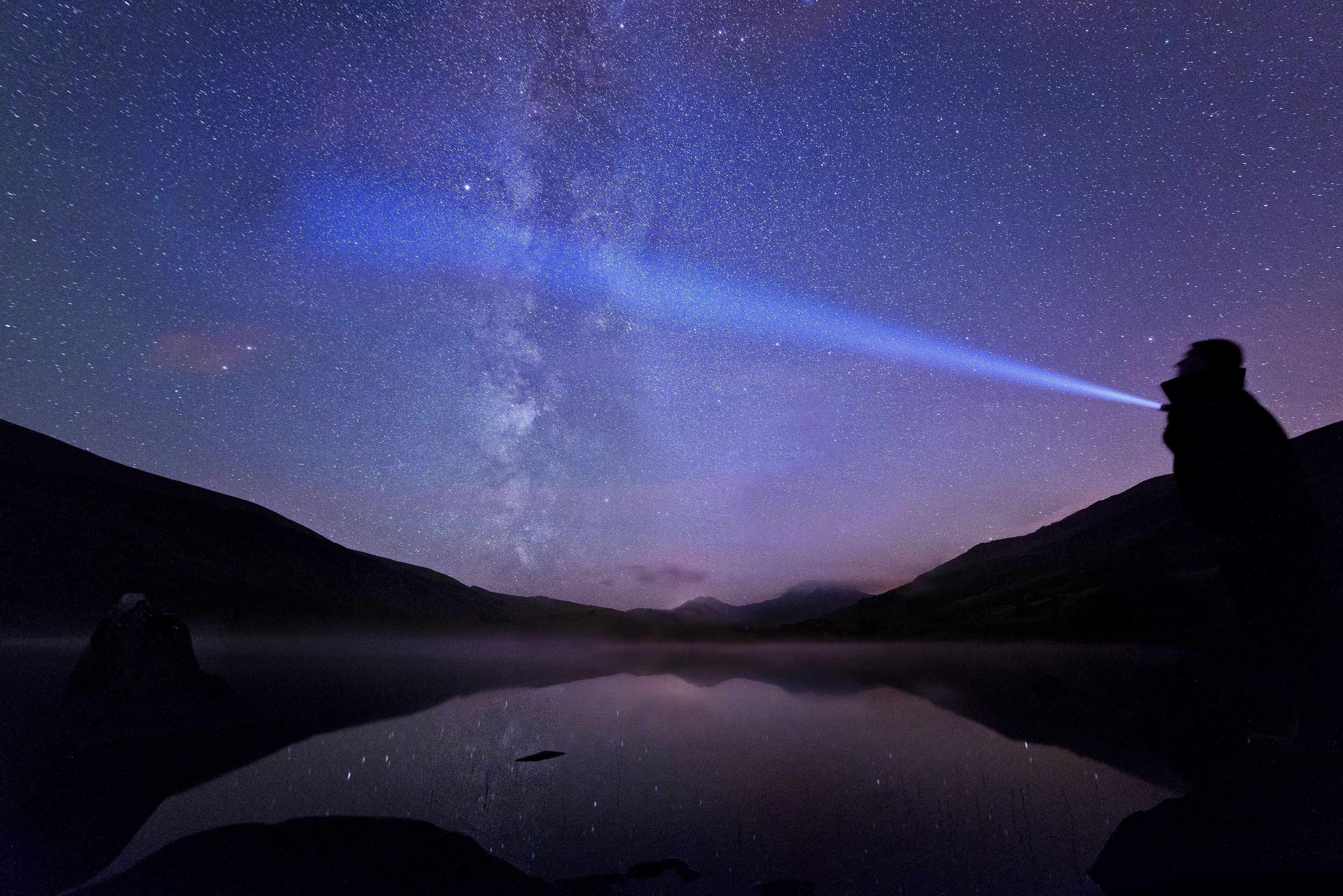 Un ciel étoilé au-dessus d’un lac paisible, bordé de montagnes de chaque côté.
