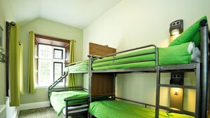Une chambre avec un lit superposé, une literie verte, une fenêtre avec des rideaux et une tête de lit en bois.