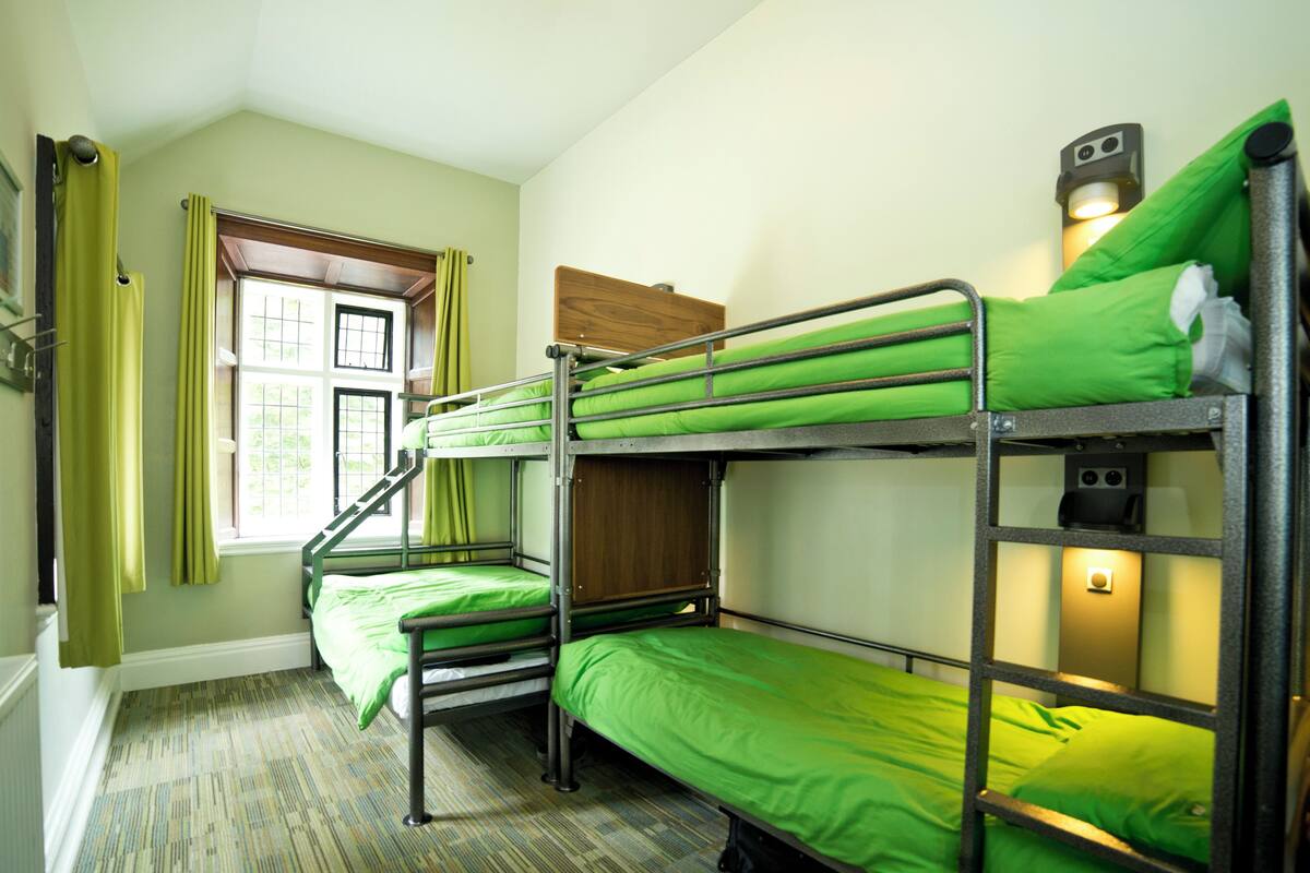 A bunk bed room with green bedding, a window with curtains, and a wooden headboard.