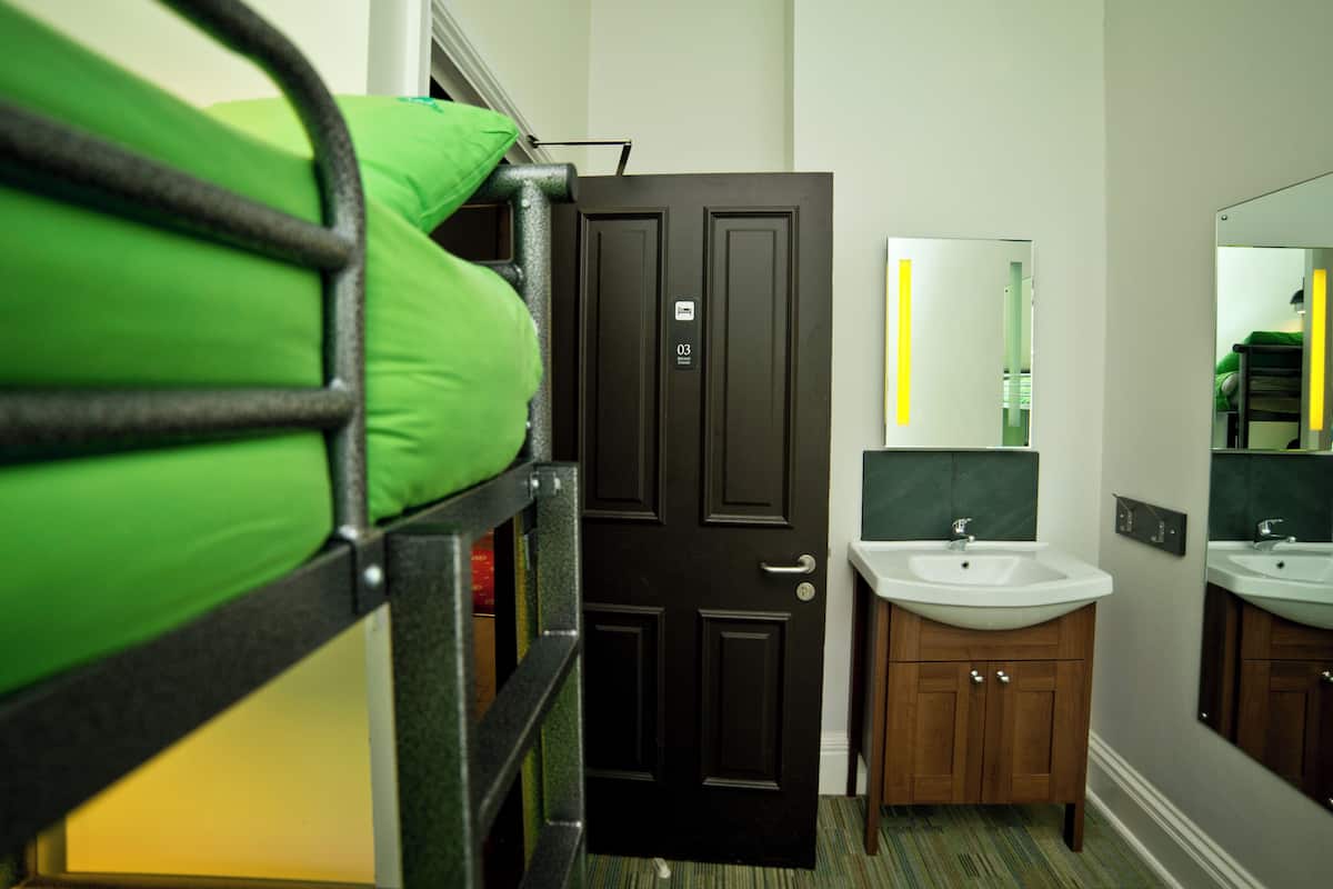 A hotel room with a bunk bed, a door with a number, a sink, and a mirror.