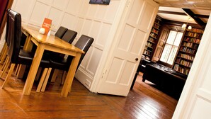 Un coin repas avec une table en bois et des chaises noires, une bibliothèque remplie de livres et une porte donnant sur une autre pièce.