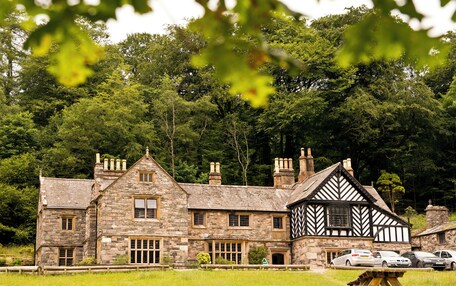 A stone building with a mix of traditional and Tudor-style architecture, featuring multiple chimneys and a large lawn in front.