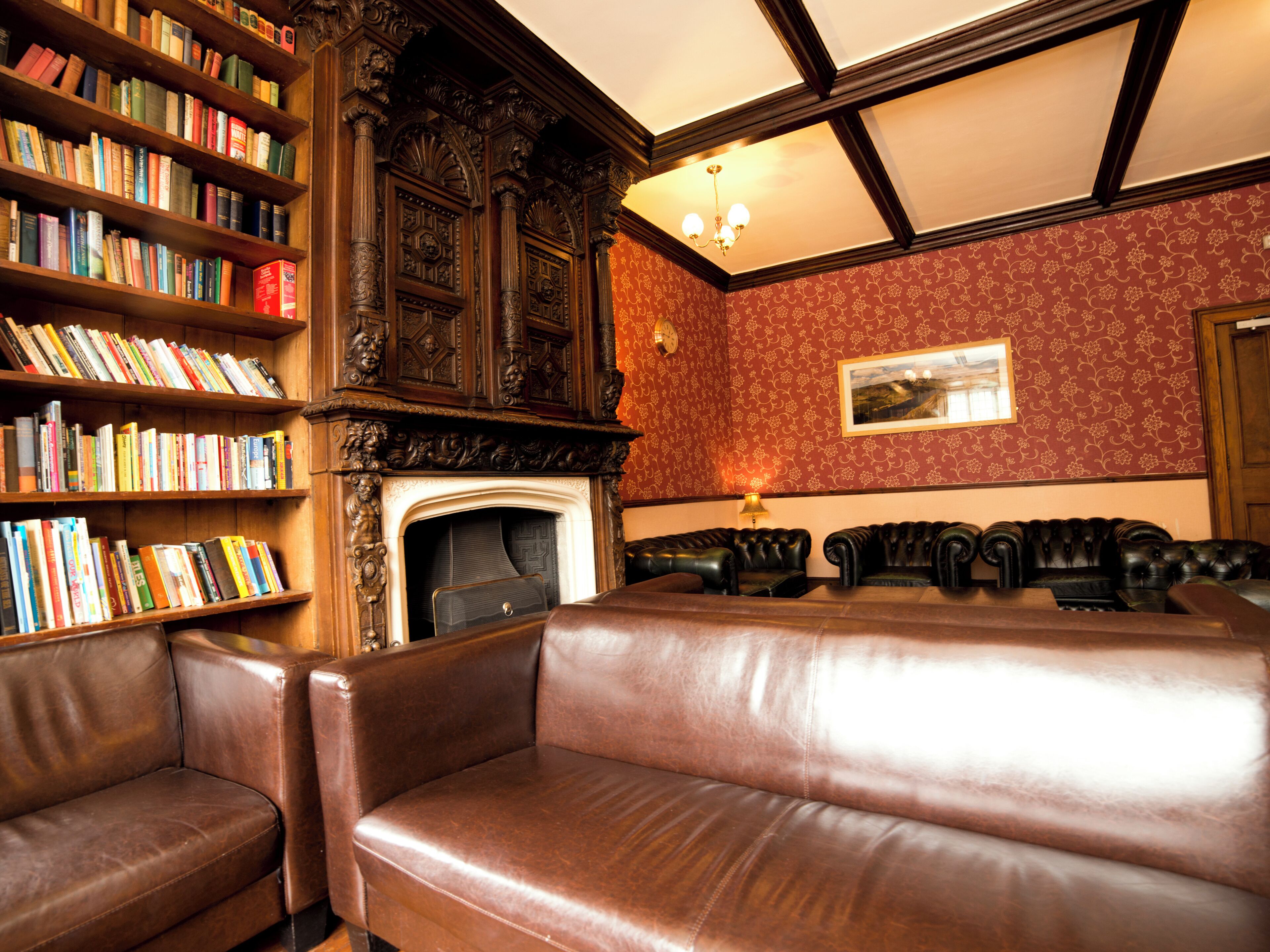Una biblioteca con estanterías, chimenea, sofás de cuero y un papel tapiz estampado.