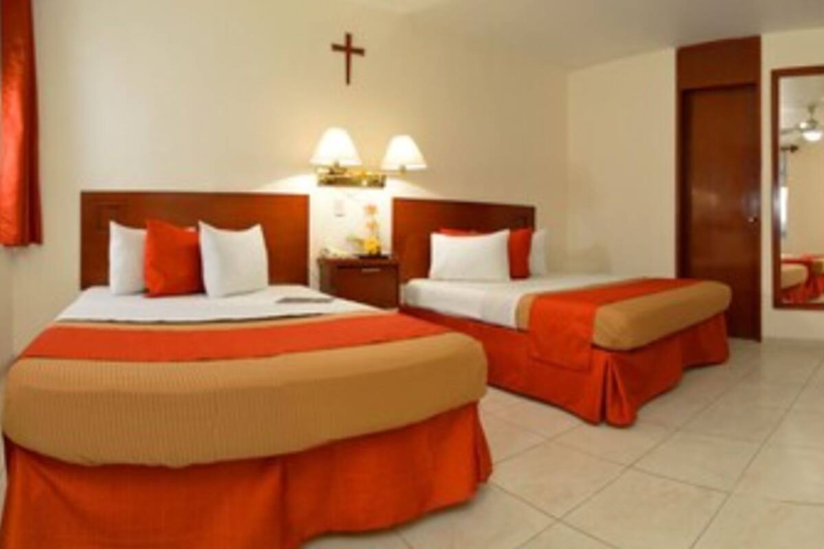 A hotel room with two beds, a nightstand with lamps, a wardrobe, and a cross on the wall.