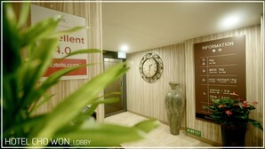 Una hall d'albergo con orologio, un vaso e una bacheca informativa.