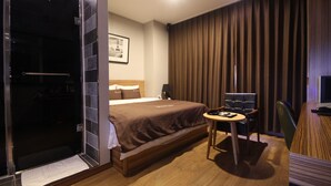 Quarto de hotel com cama, escrivaninha, cadeira, guarda-roupa e uma janela grande com cortinas.