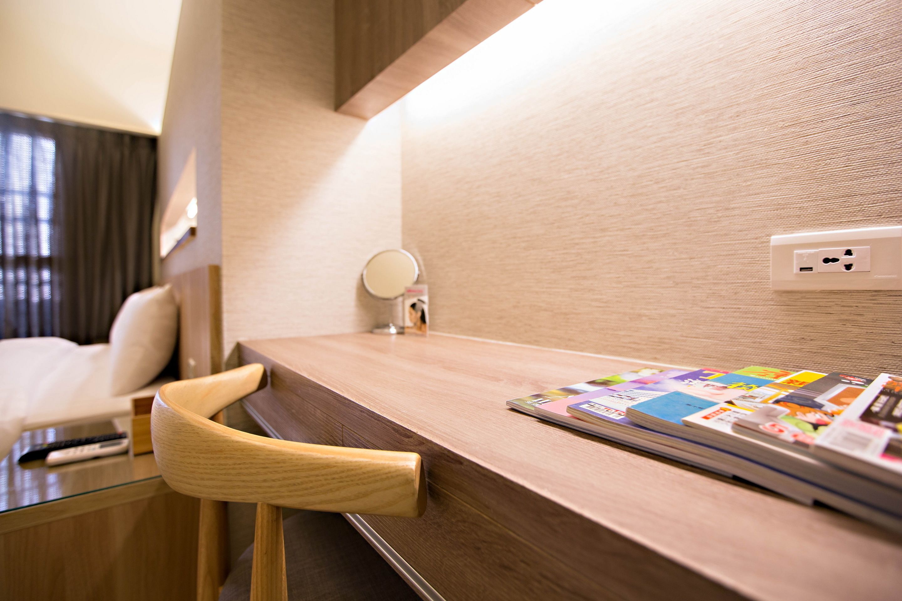 A wooden desk with a magazine, a remote control, and a wall socket.