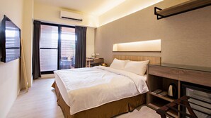 A modern hotel room with a large bed, a desk, a flat-screen TV, and a sliding glass door to the balcony. - Traveller Inn Book Haus (Taitung)