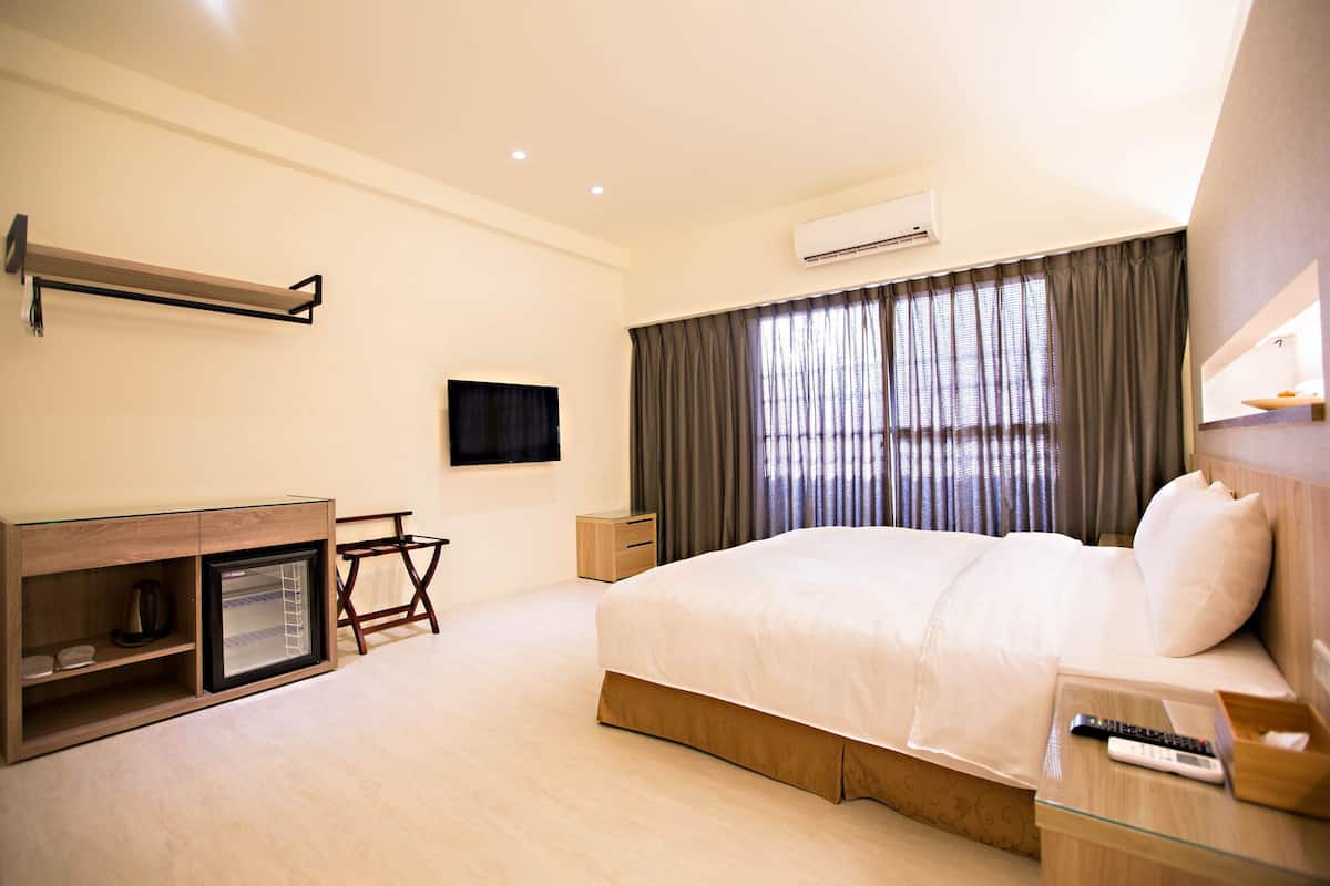 A hotel room with a bed, bedside table, TV, and a small desk with a chair.