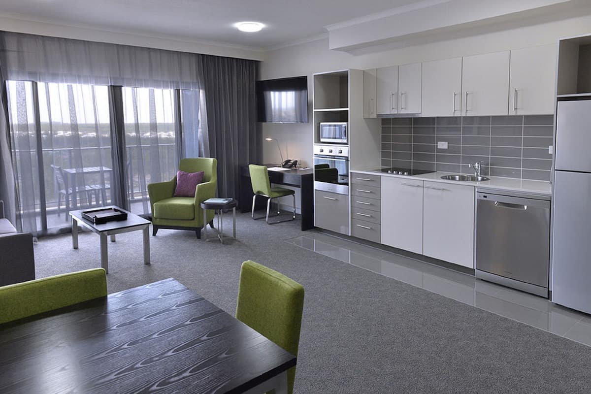 A modern hotel room with a dining area, a kitchenette, and a view of the city.