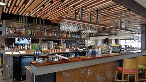 A modern bar area with a wooden ceiling, multiple shelves of bottles, and a variety of bar tools.