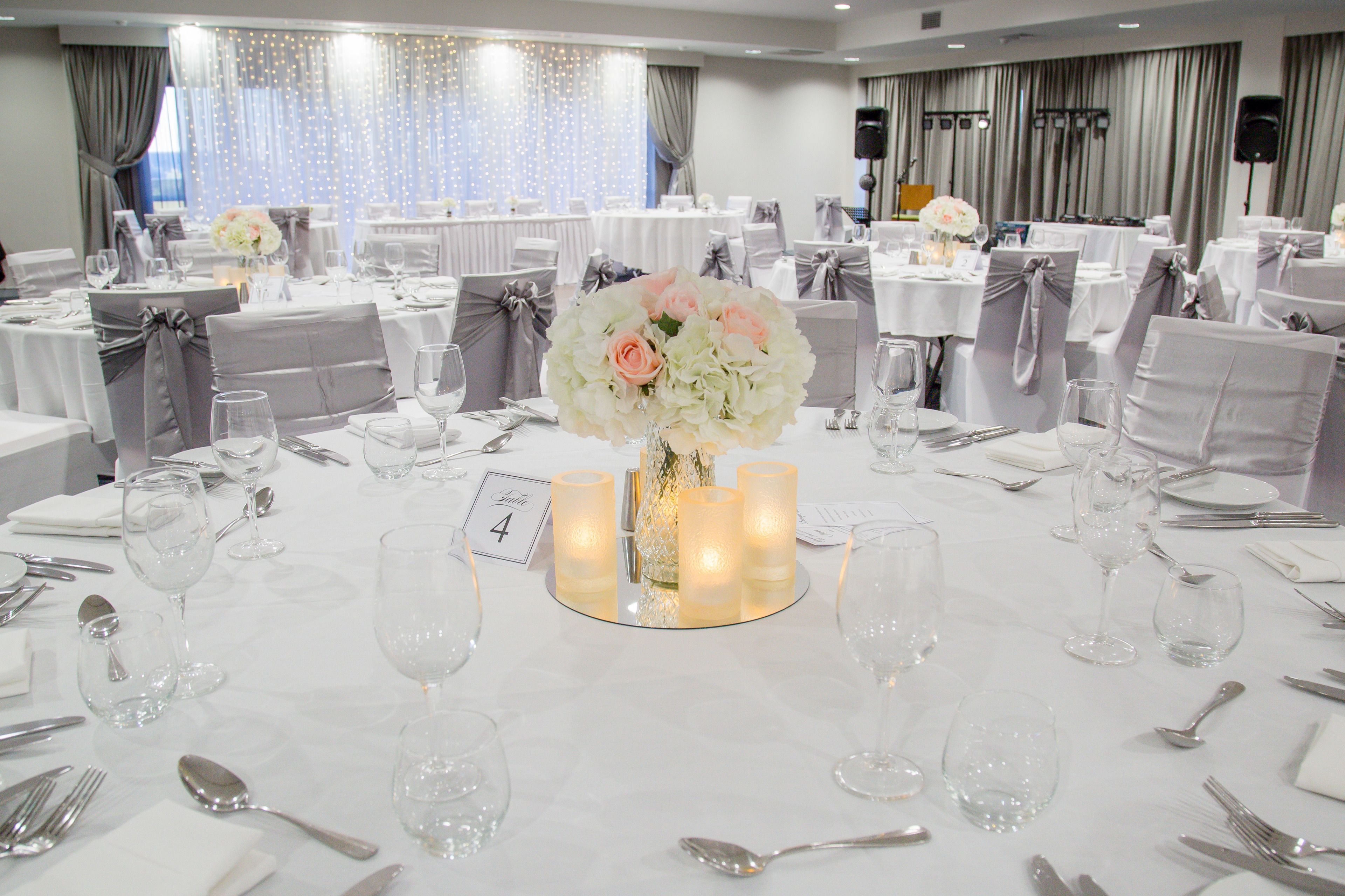 A banquet hall with round tables, each set with white tablecloths, silverware, and glassware.