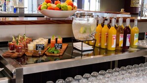 A buffet bar with a variety of food and drink options, including a bowl of fruit, a pitcher of iced tea, and several bottles of juice.