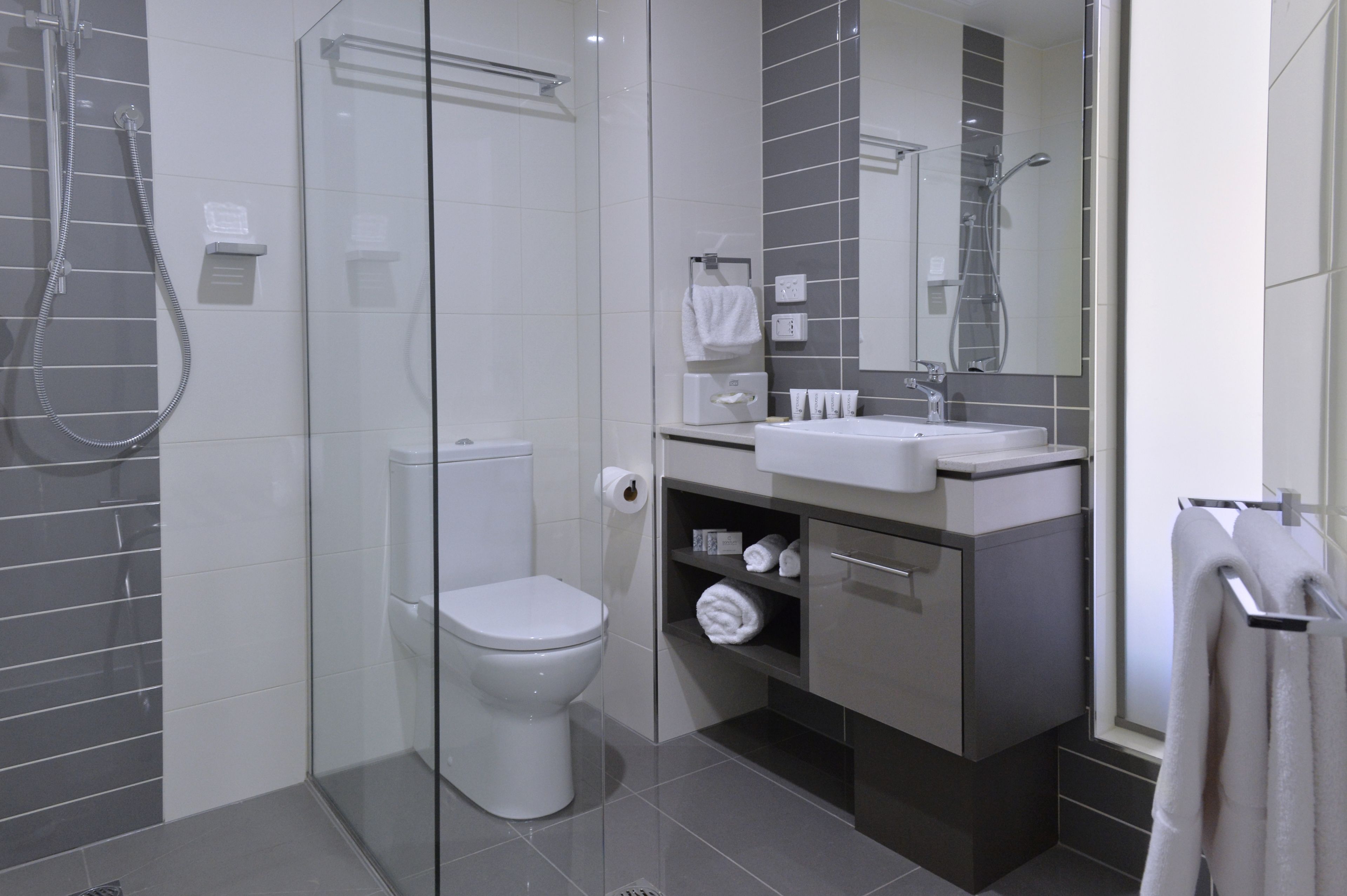 A modern bathroom with a glass-enclosed shower, a toilet, and a vanity with a mirror.