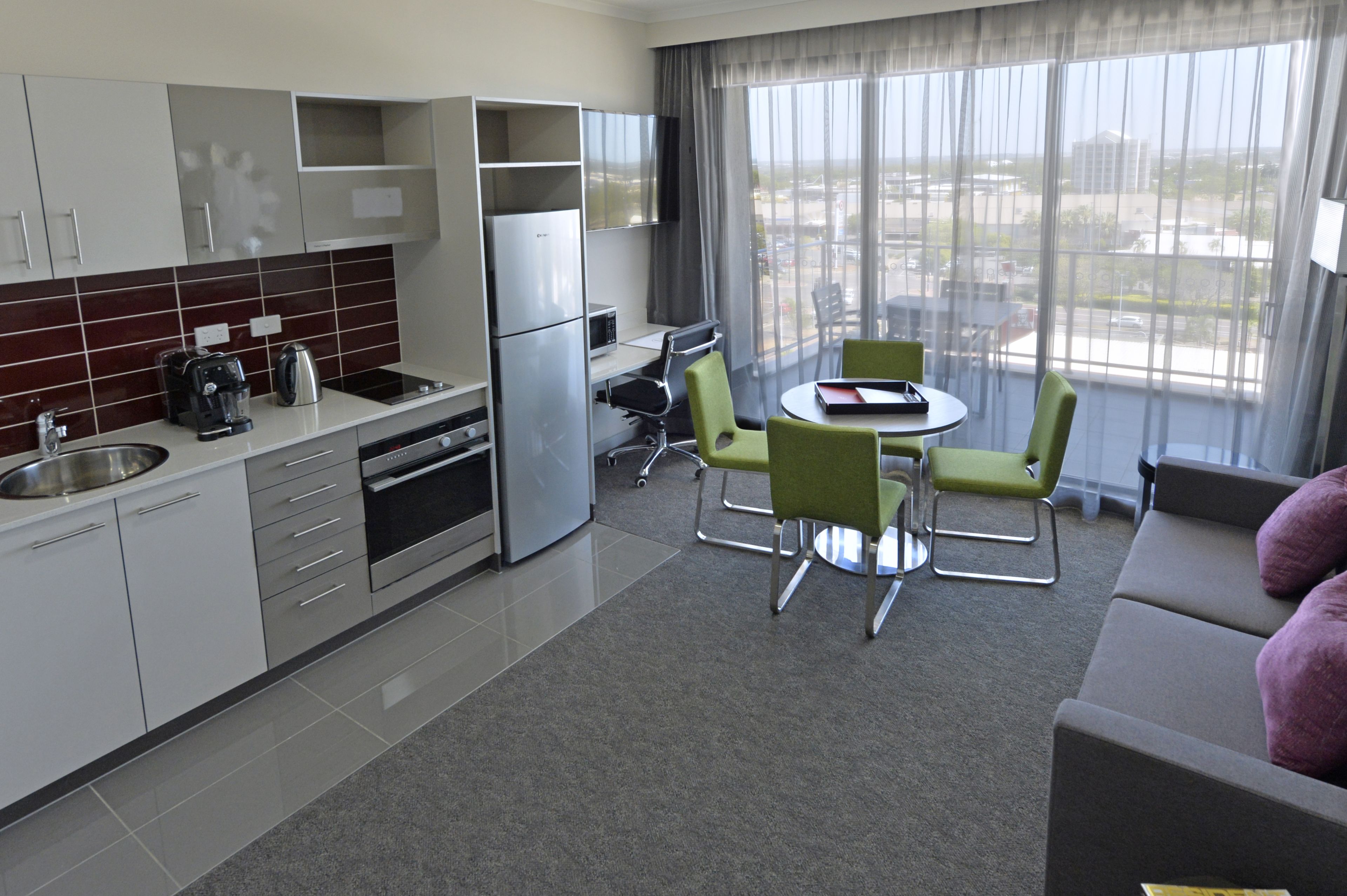 A modern hotel room with a kitchen, dining area, and a balcony with a view.