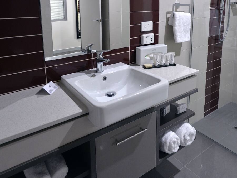 A modern bathroom with a white sink, a mirror, a towel rack, and a shower area.