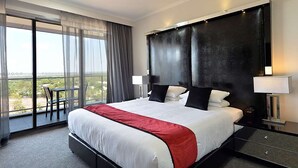 A hotel room with a large bed, a balcony with a chair, and a view of the city.