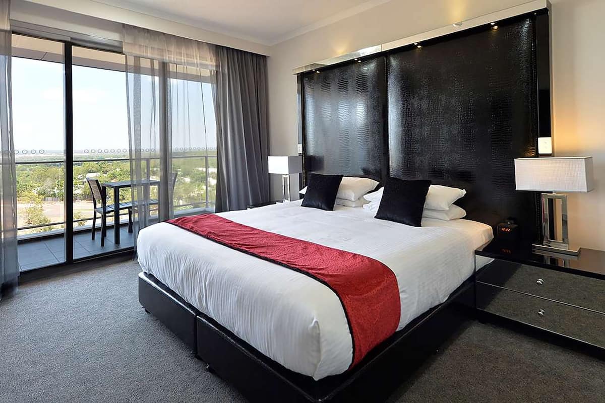 A hotel room with a large bed, a balcony with a chair, and a view of the city.