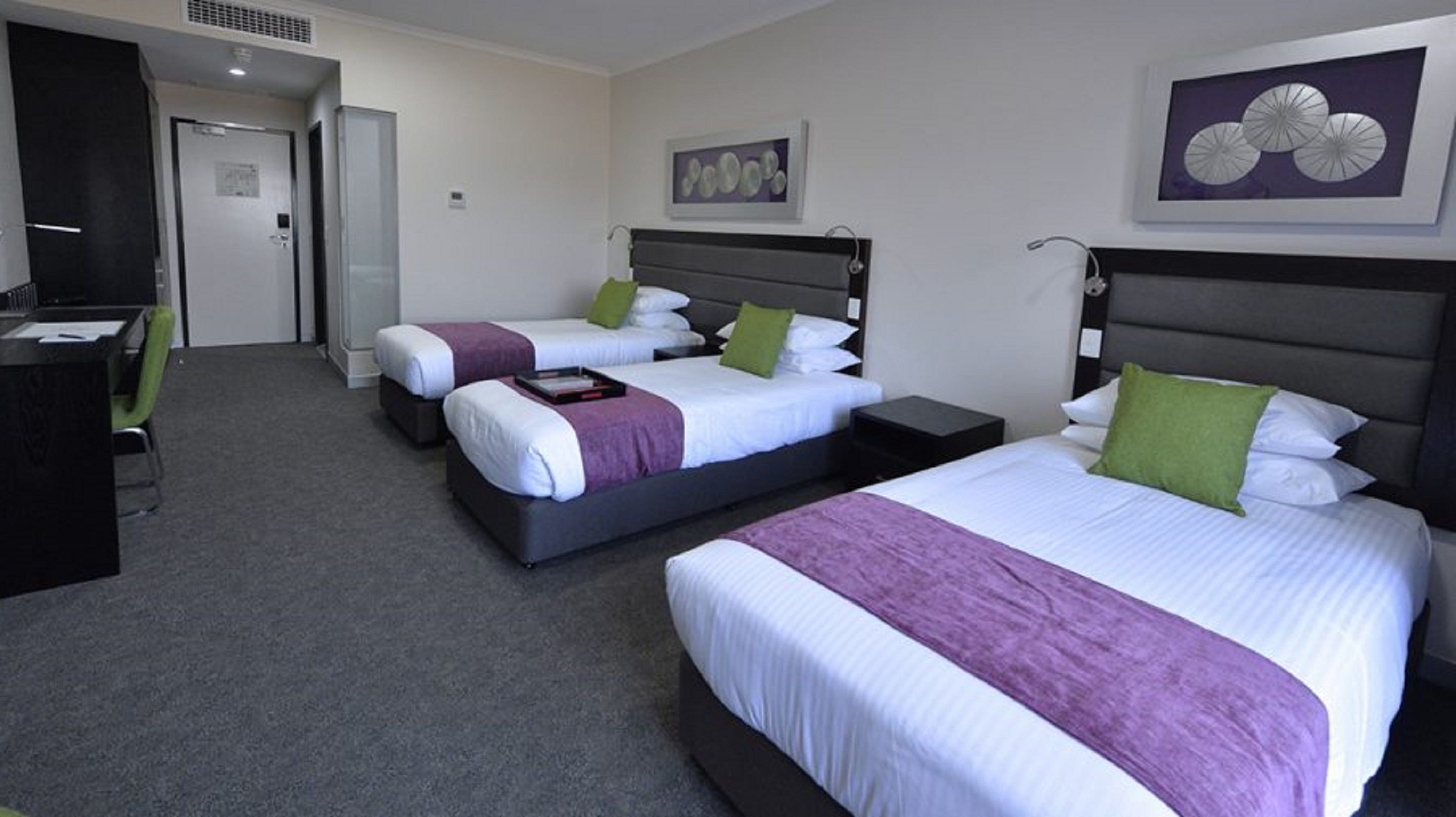 A hotel room with two beds, a desk, and a chair. There are two paintings on the walls.