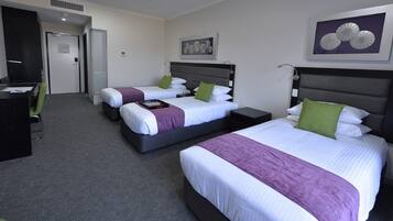 A hotel room with two beds, a desk, and a chair. There are two paintings on the walls.