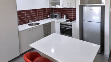 A modern kitchen with white cabinets, a stainless steel sink, a microwave, a kettle, and a refrigerator.