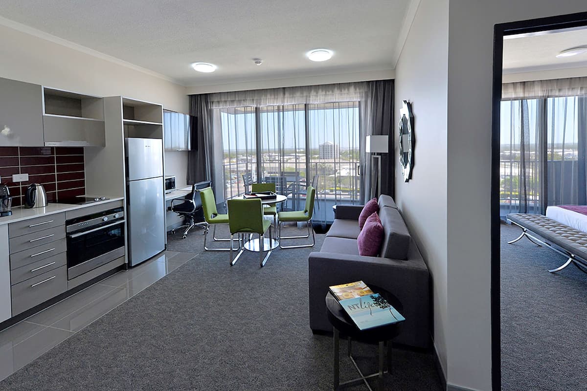 A modern hotel room with a kitchenette, dining area, and a balcony with a city view.