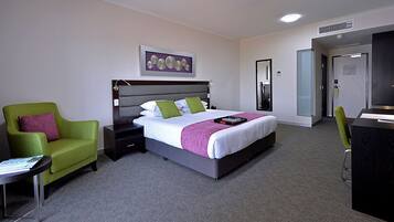 A hotel room with a bed, a green armchair, a desk, and a mirror.