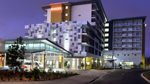 A modern hotel with a distinctive geometric facade, multiple balconies, and a car park.