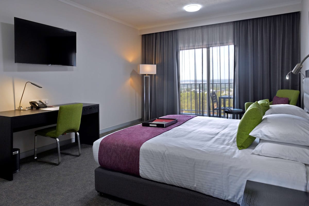 A hotel room with a bed, a desk, a chair, a TV, and a window with curtains.
