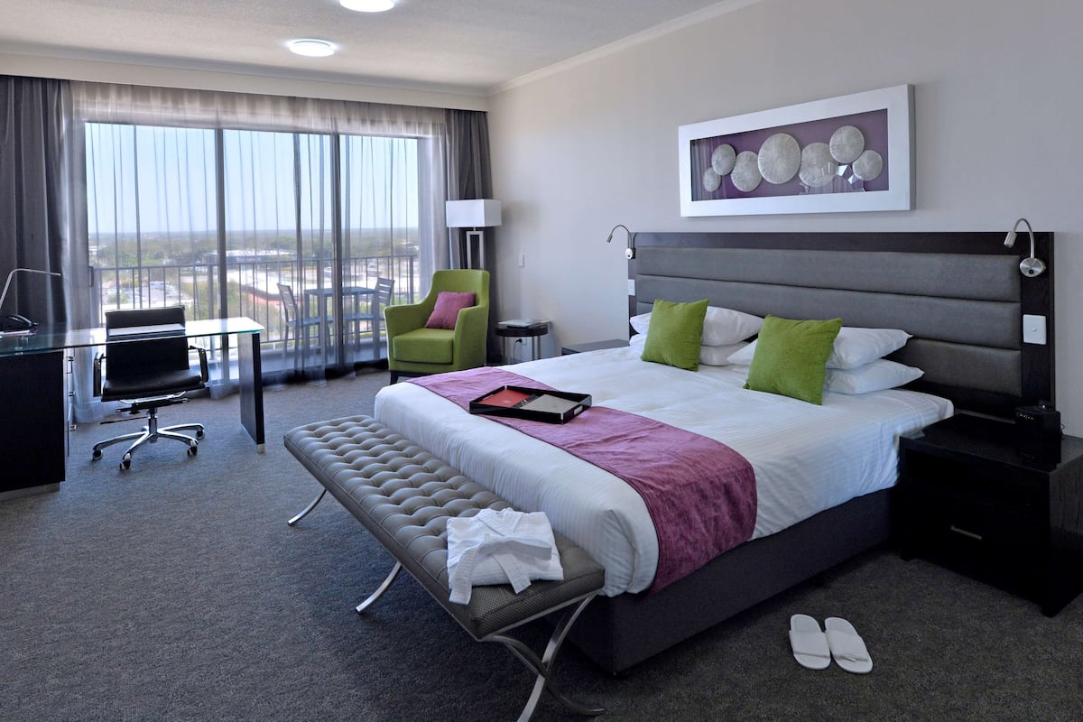 A hotel room with a large bed, a desk, a chair, and a view of the city.