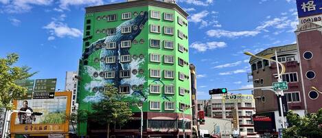 A multi-story building with a green facade and a mural of a bird.