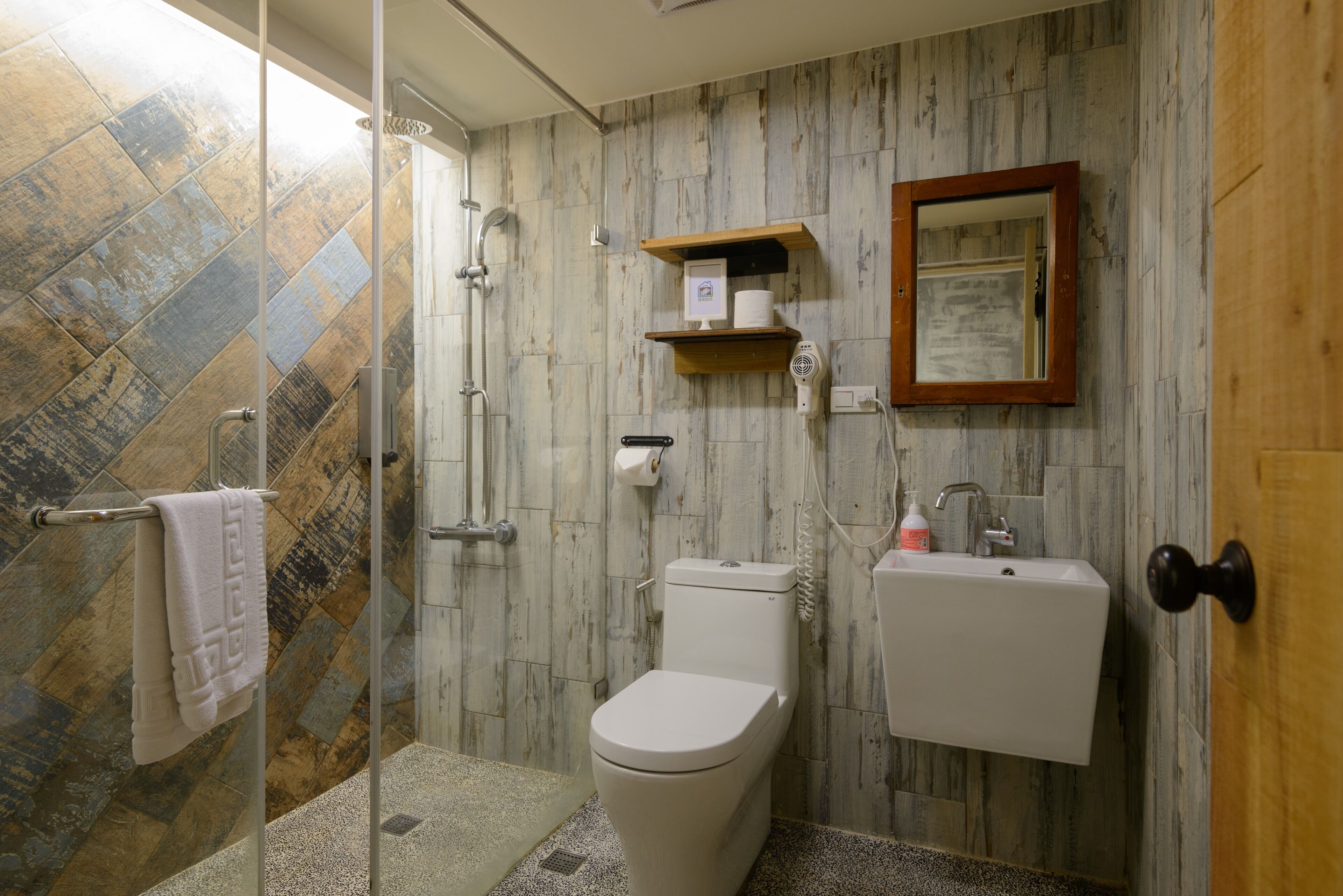 A bathroom with a shower, toilet, sink, and a wooden shelf with toiletries.