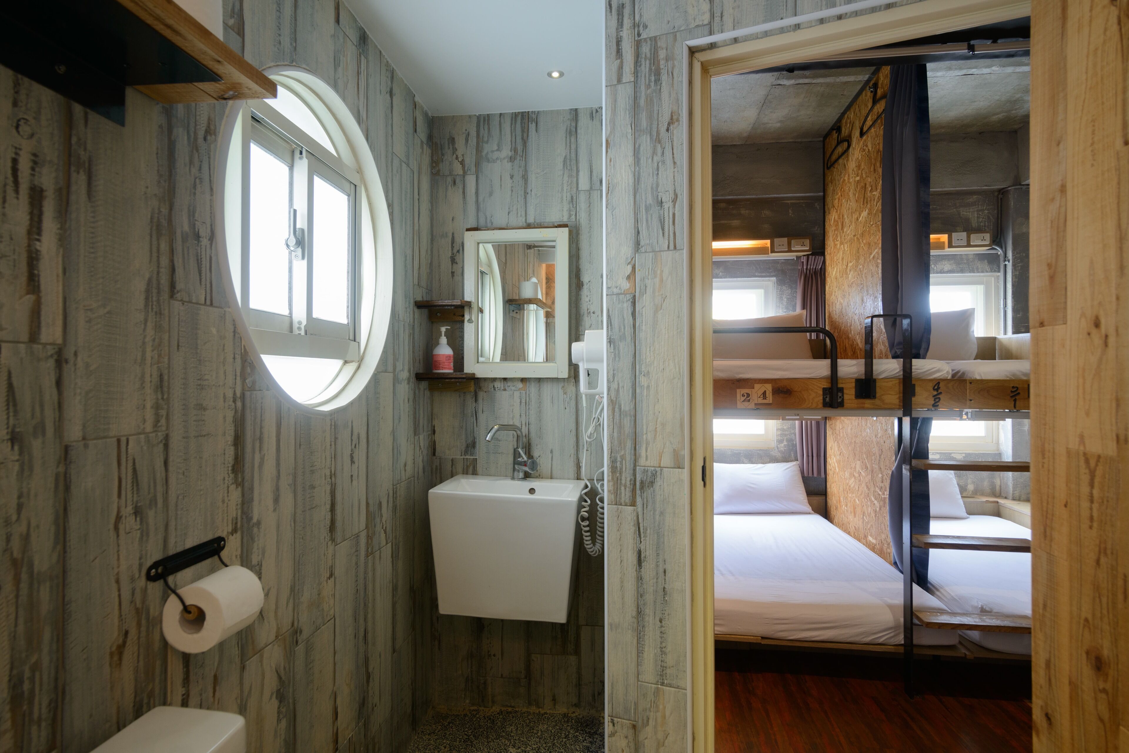 A compact room with a bunk bed, a small sink, and a round window.