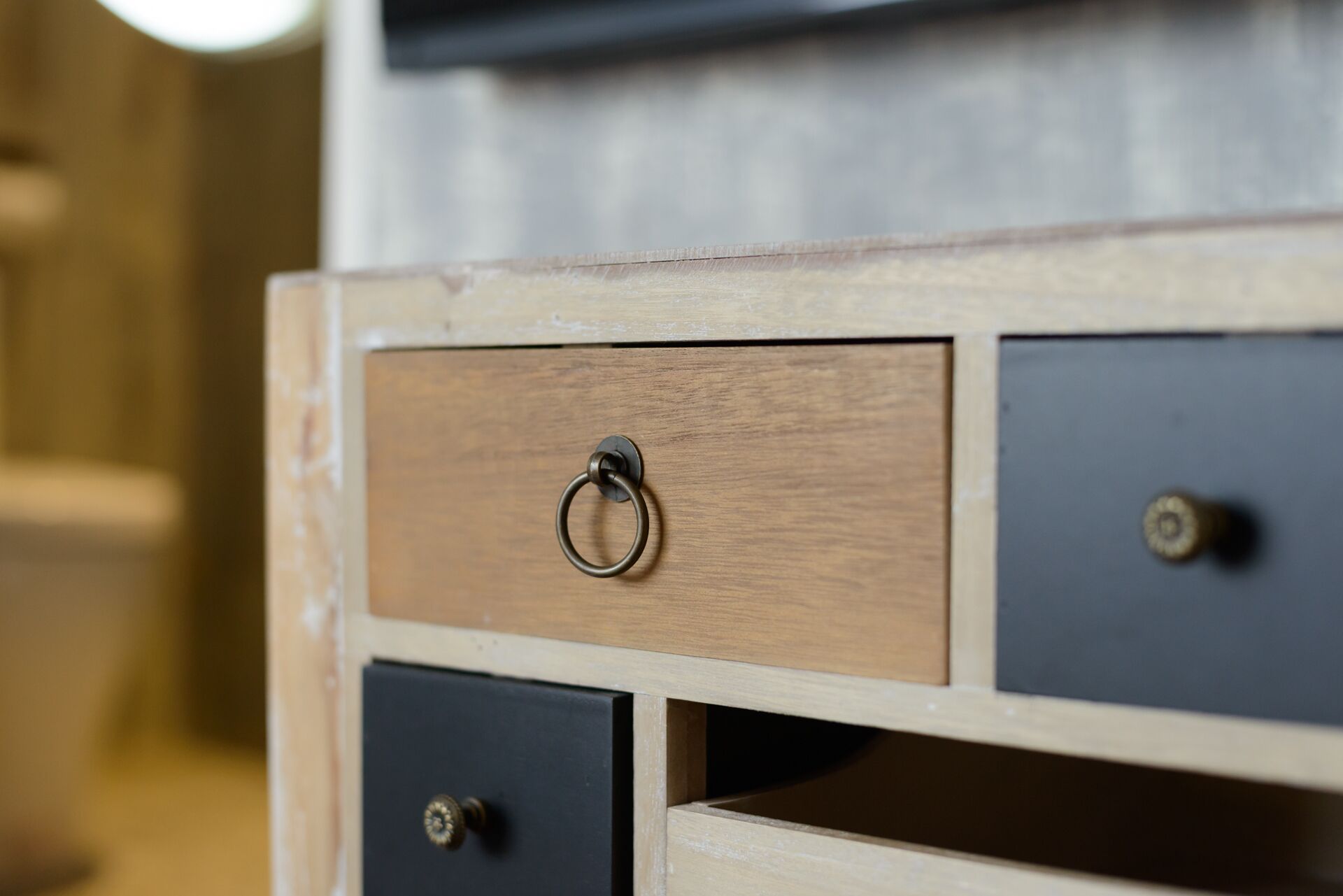 Cómoda de madera con un cajón de tipo palanca, un cajón negro y un estante visible en la parte inferior.