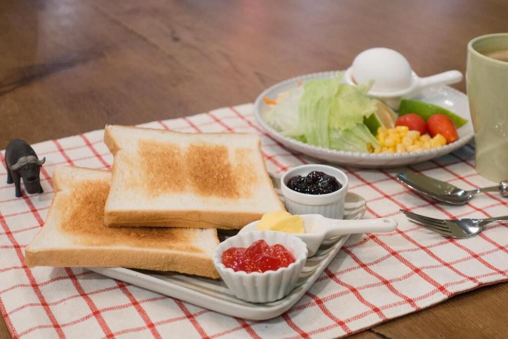 Ein Frühstückstisch mit Toast, Marmelade, Butter und einem Salat auf karierter Tischdecke.