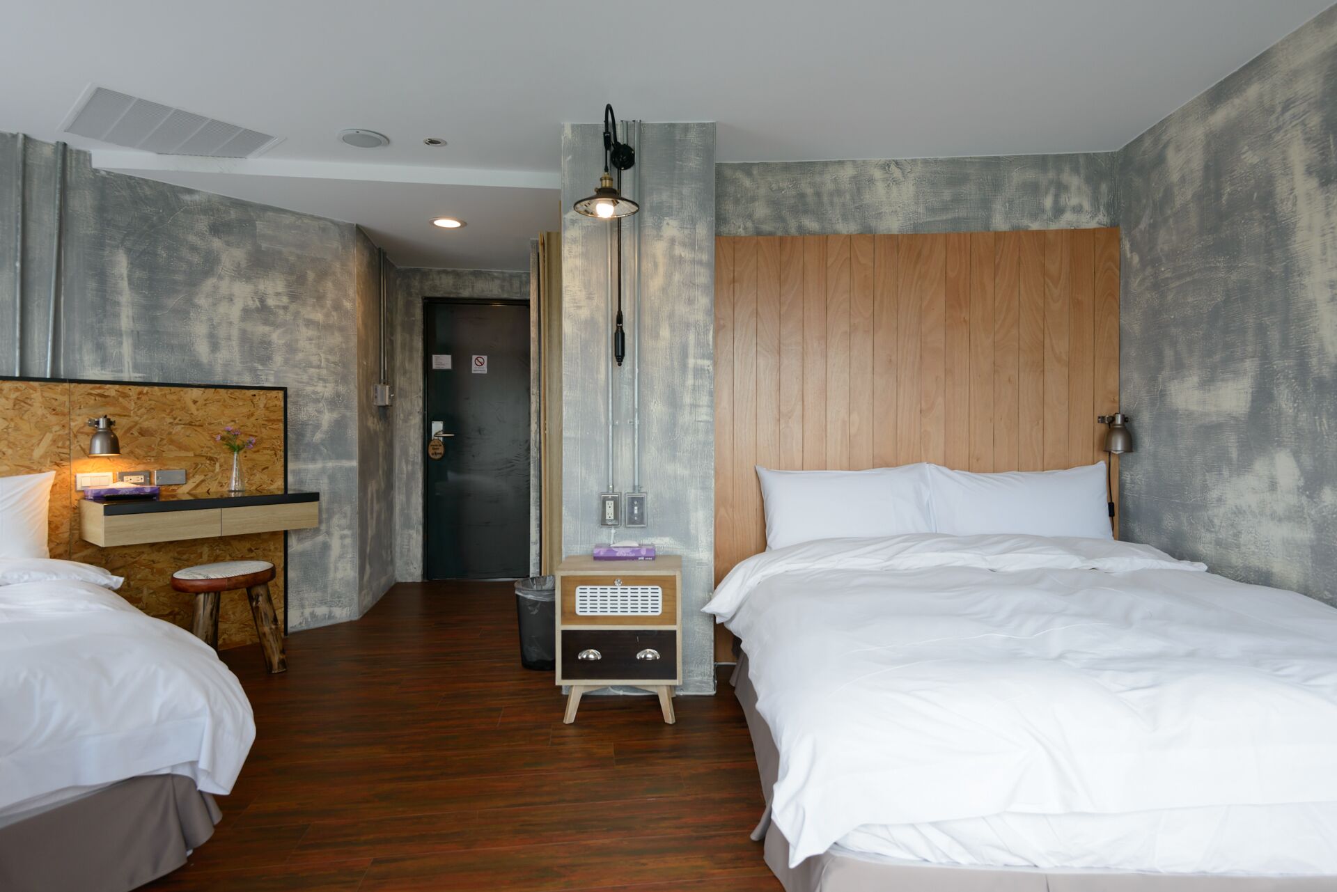 Une chambre d’hôtel avec deux lits, une tête de lit en bois, un bureau avec une lampe et un grand miroir.
