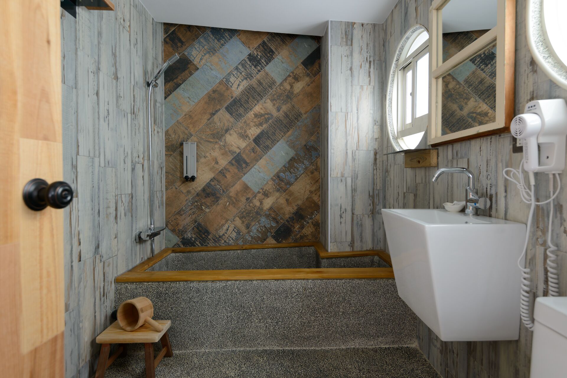 Ein Badezimmer mit Wandpaneelen in Fischgrätmuster, einer Holztür, einem Waschbecken mit Spiegel und einem Fön.