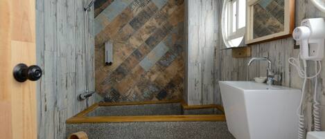 A bathroom with a herringbone-patterned wall, a wooden door, a sink with a mirror, and a hairdryer.