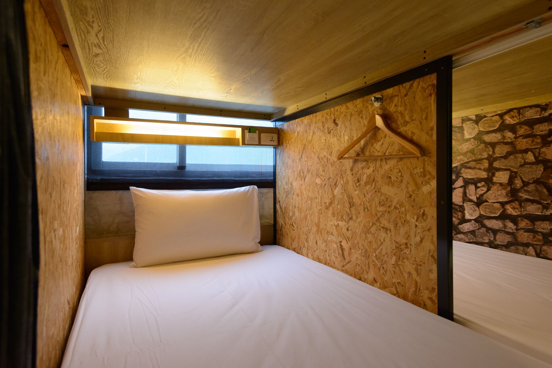 Una cama individual con colchón y almohada blancos en una habitación con paredes de madera y una sección de pared de piedra.