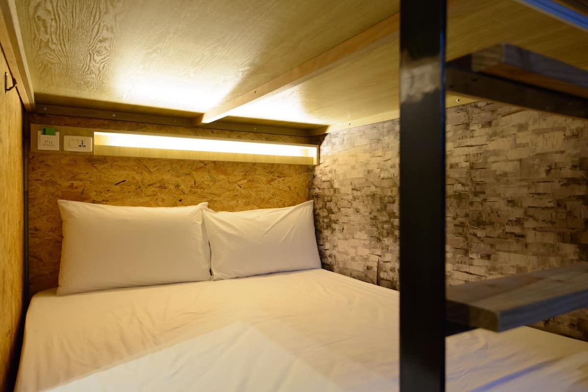 Uma cama beliche com roupa de cama branca num quarto com teto de madeira e parede de tijolos.