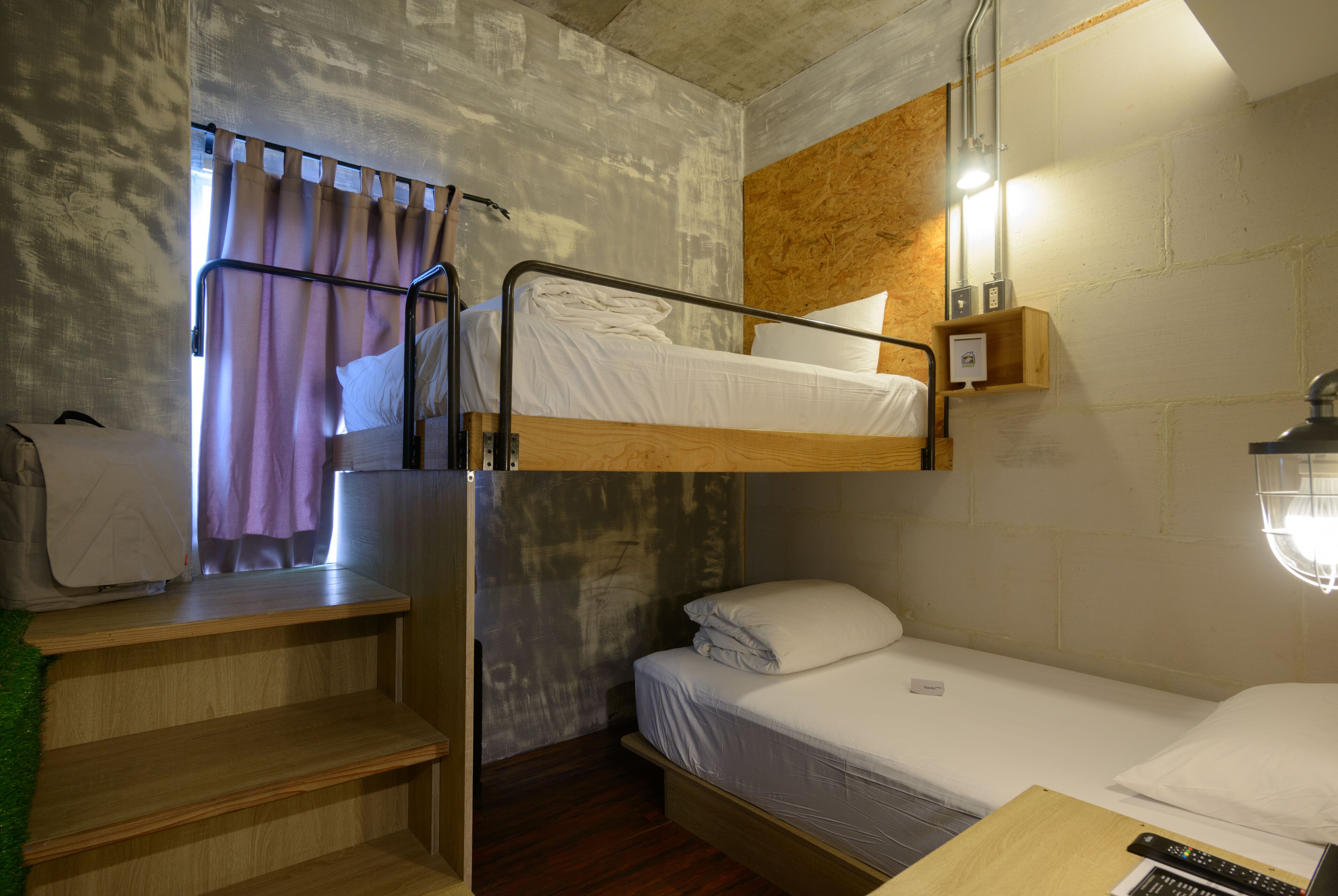 A bunk bed room with a wooden desk, a small shelf, and a window with curtains.