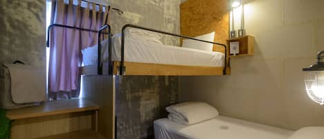 A bunk bed room with a wooden desk, a small shelf, and a window with curtains.